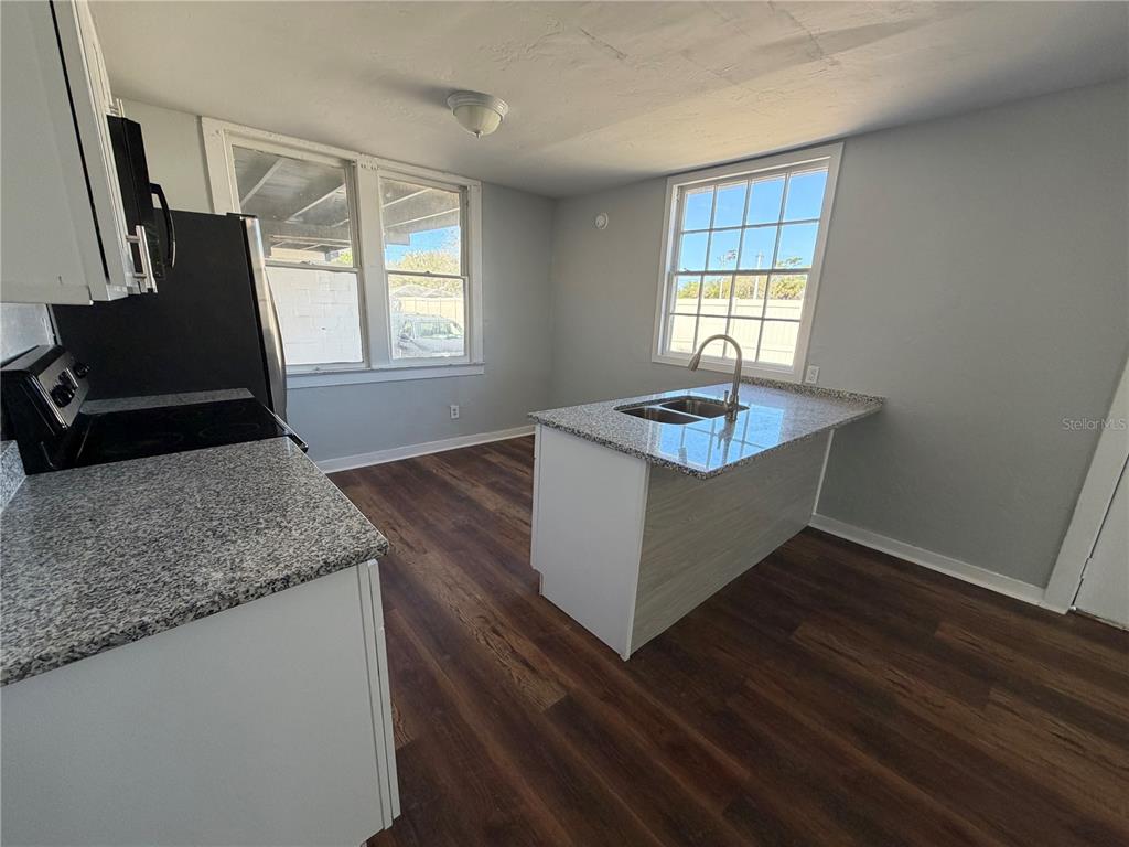 A kitchen features a granite-topped island, stainless steel appliances, and dark wood-look flooring — 325 S FRANKLIN STREET, DAYTONA BEACH, FL