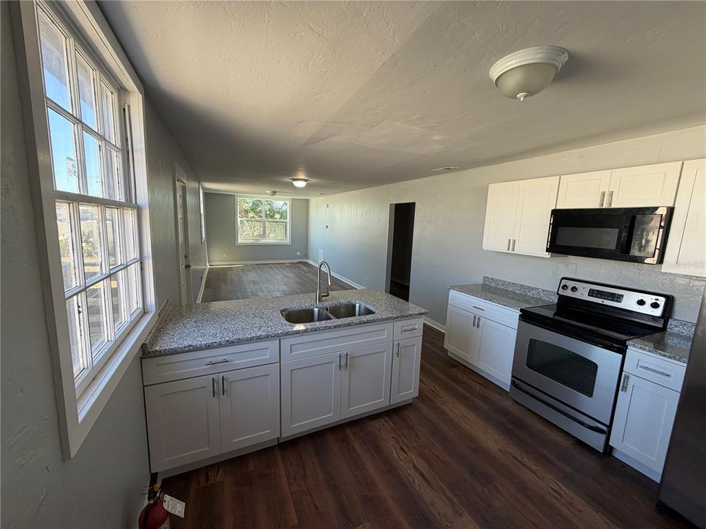 A kitchen with white cabinets, granite countertops, and stainless steel appliances overlooks a living area — 325 S FRANKLIN STREET, DAYTONA BEACH, FL
