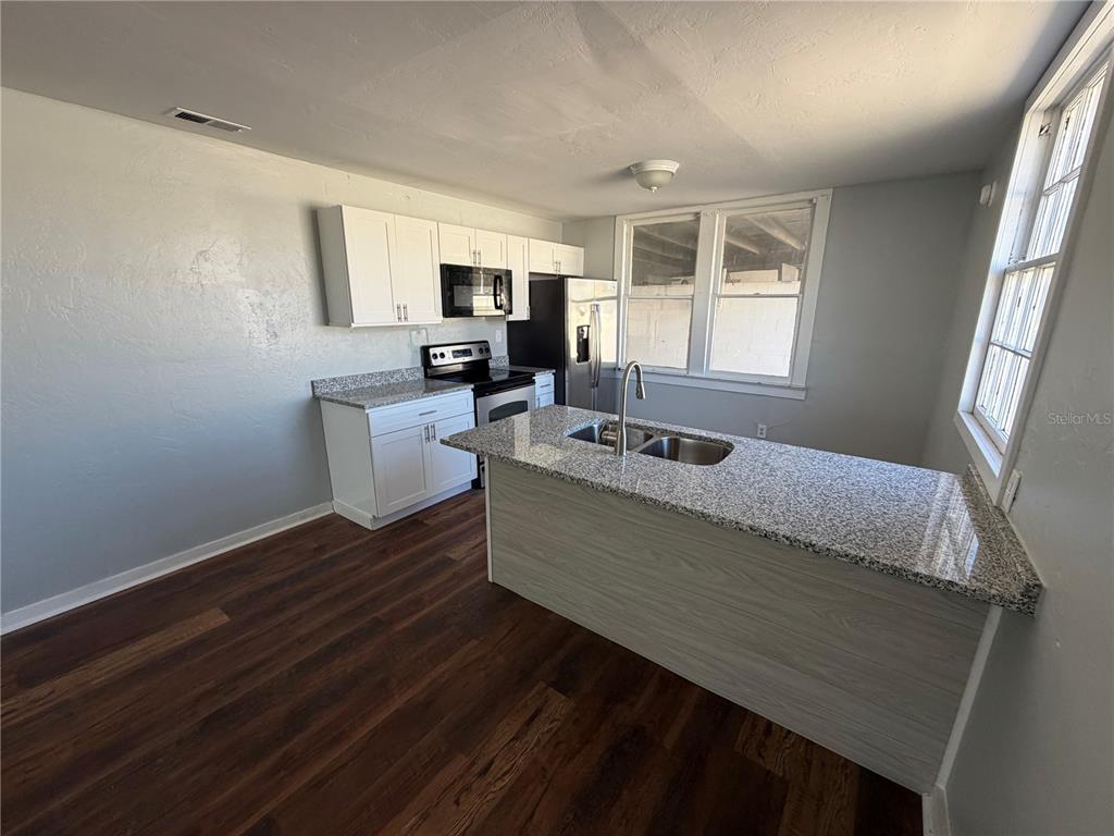 A kitchen features white cabinets, granite countertops, a stainless steel sink, and wood-look flooring — 325 S FRANKLIN STREET, DAYTONA BEACH, FL