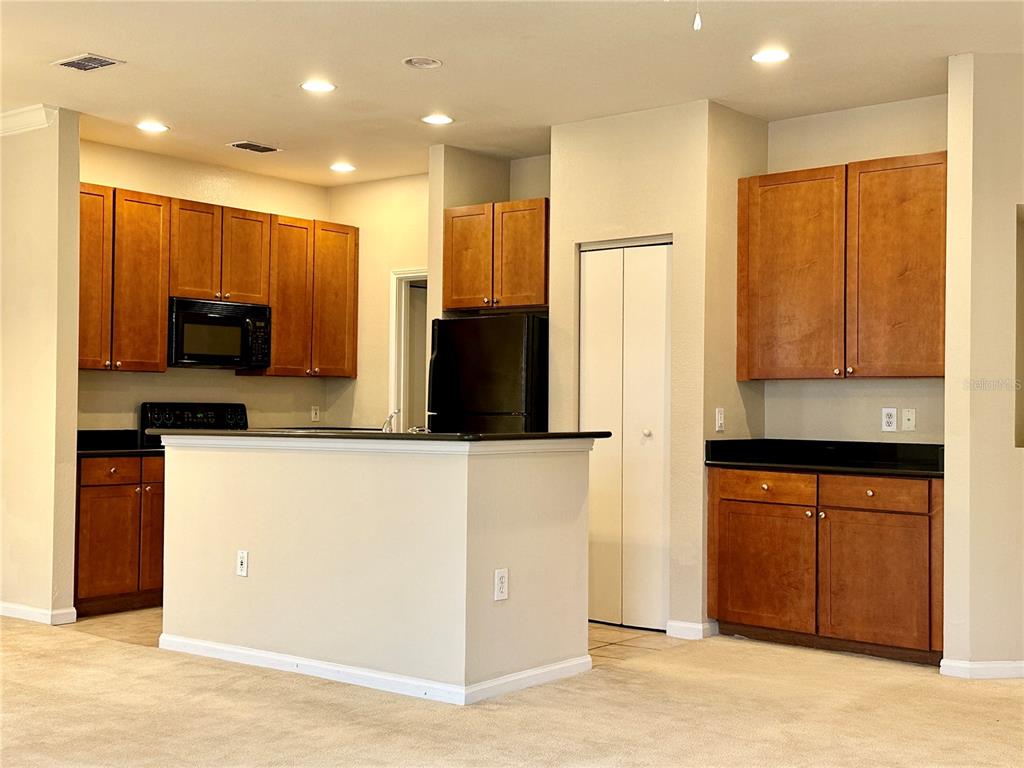 A kitchen features wood cabinets, black countertops, a center island, and black appliances — 2249 PORTOFINO PLACE UNIT 2221, PALM HARBOR, FL