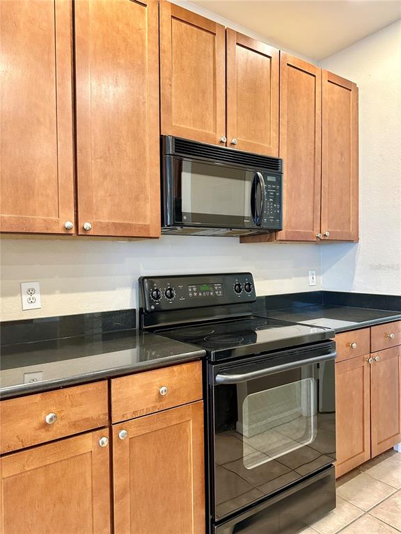A kitchen features wood cabinets, black countertops, and a black stove with a microwave above — 2249 PORTOFINO PLACE UNIT 2221, PALM HARBOR, FL