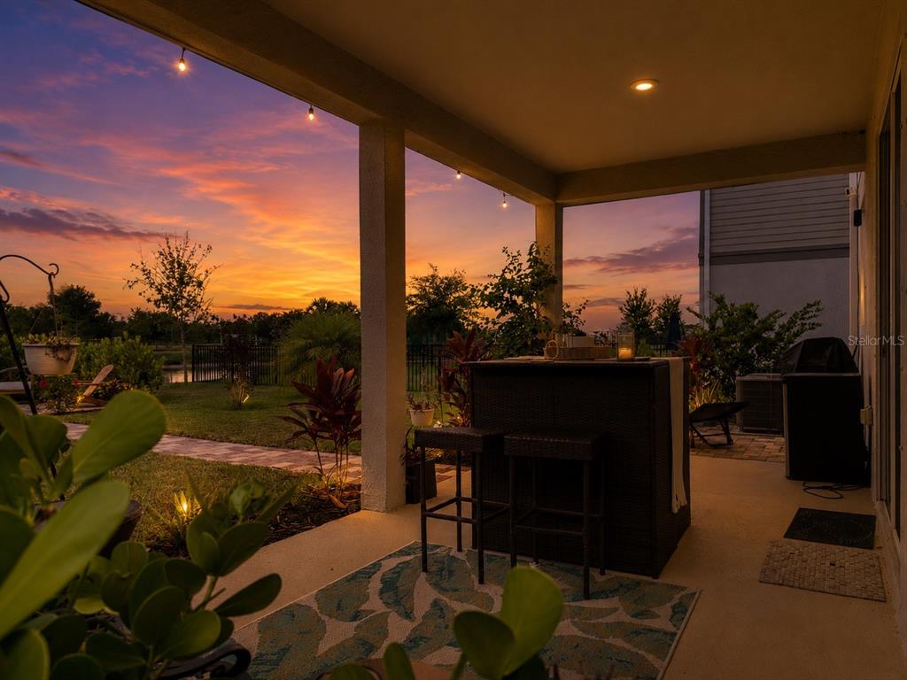 A covered patio features a bar set, outdoor lighting, and a view of a sunset — 11567 GALLATIN TRAIL, PARRISH, FL