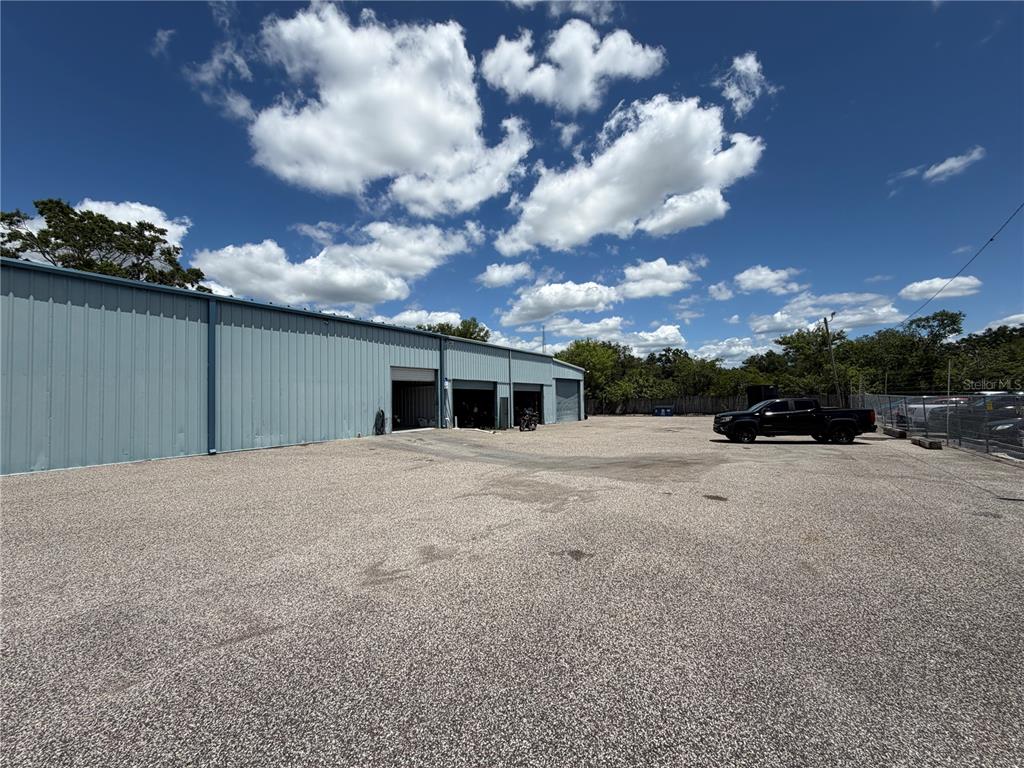 A metal warehouse building sits on a large gravel lot under a blue sky — 15921 N FLORIDA AVENUE, LUTZ, FL