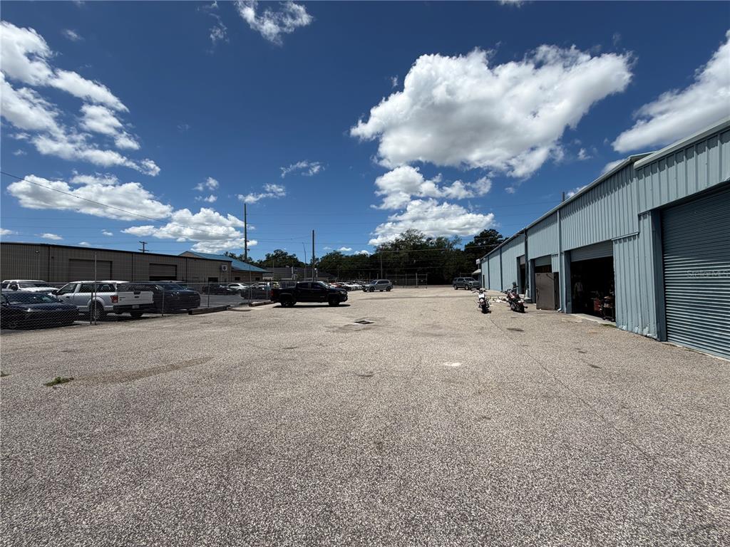 A large, paved outdoor parking lot sits between two industrial warehouse buildings under a blue sky — 15921 N FLORIDA AVENUE, LUTZ, FL