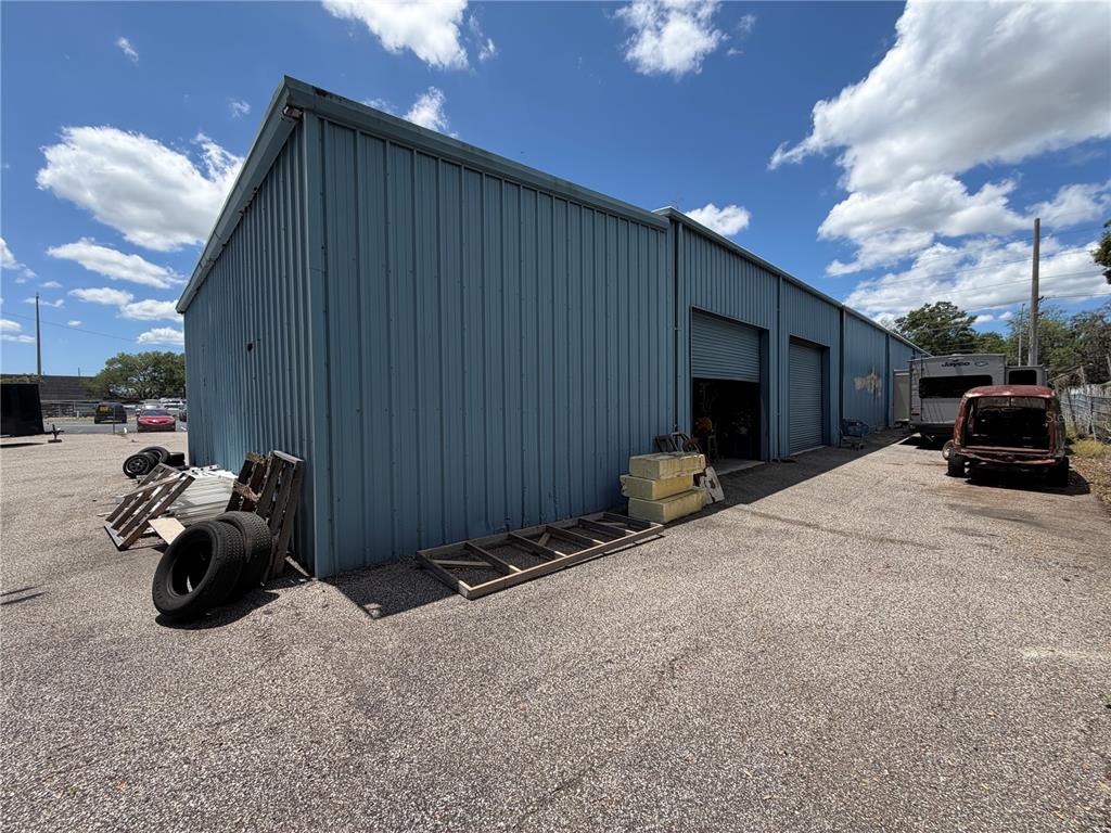 A blue metal warehouse building with two roll-up doors sits on a gravel lot — 15921 N FLORIDA AVENUE, LUTZ, FL