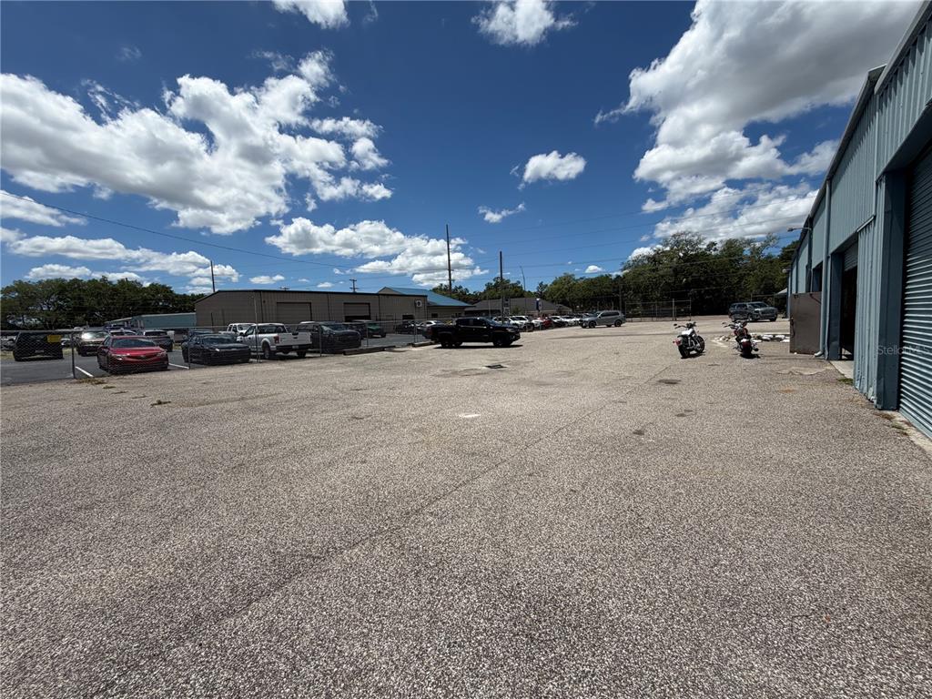 A large, paved outdoor parking lot sits beside a metal industrial building under a cloudy sky — 15921 N FLORIDA AVENUE, LUTZ, FL