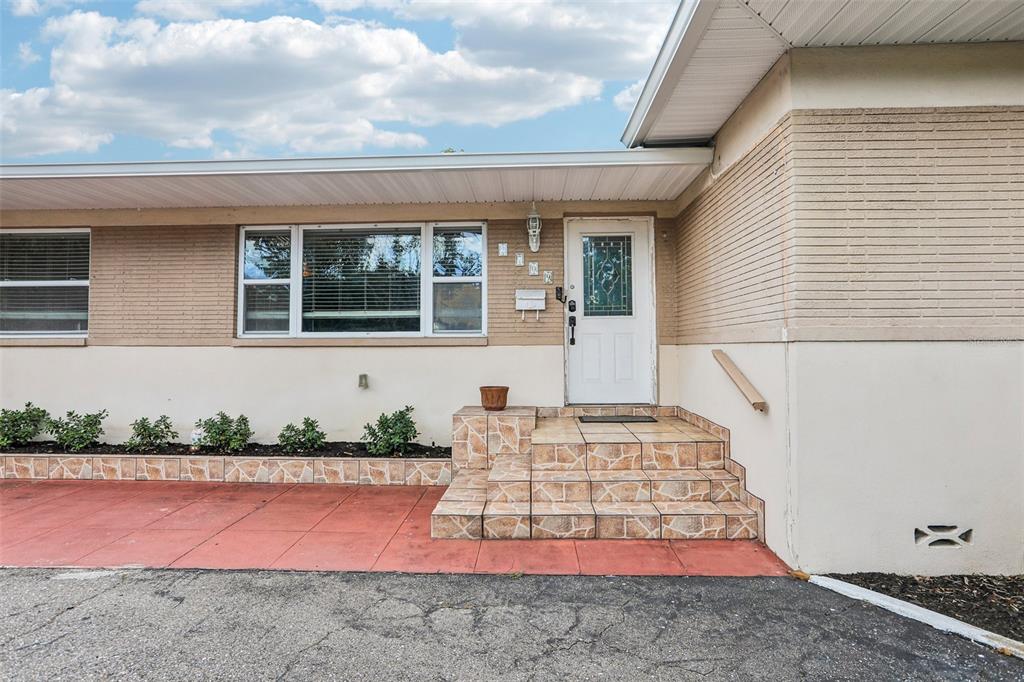 The exterior of a house features a white front door, tiled steps, and brick siding — 2709 49TH STREET N, ST PETERSBURG, FL
