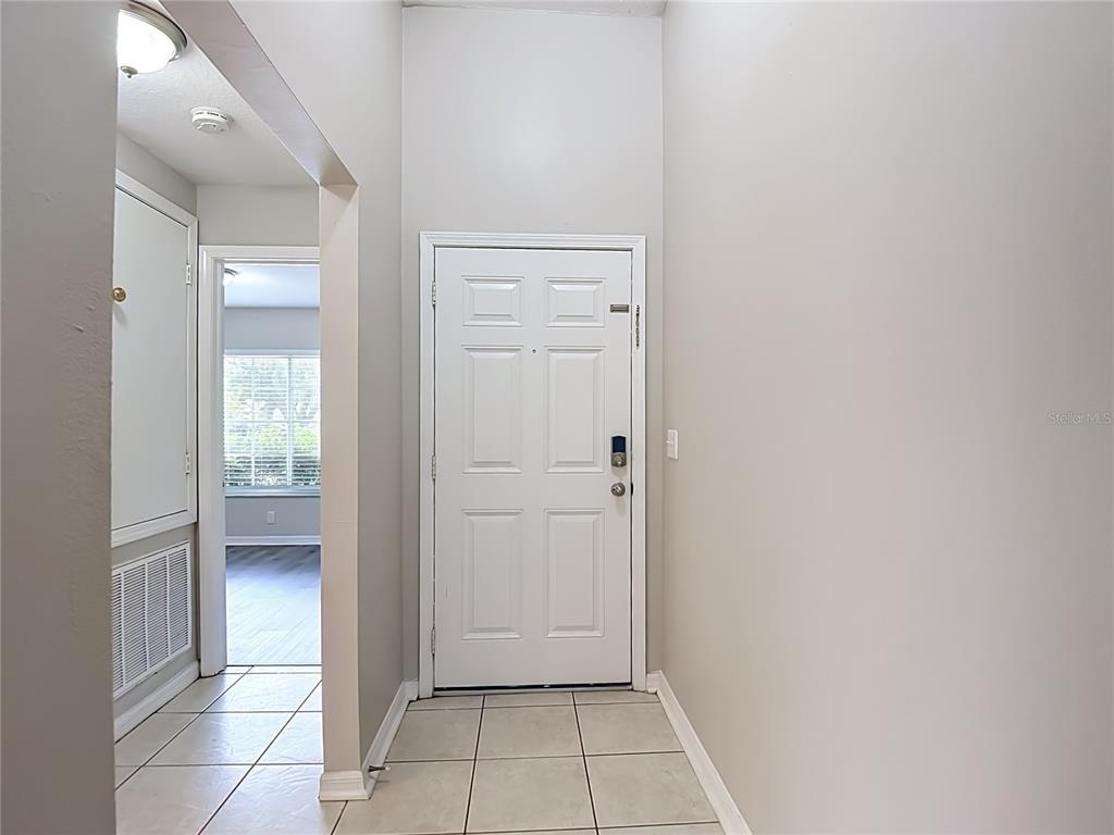 An entryway features a white front door, light-colored tile flooring, and a view into another room — 1129 CONCH COURT, WESLEY CHAPEL, FL