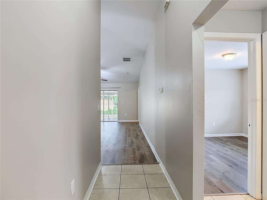 A hallway with tiled flooring leads to a living area with wood-look floors and sliding doors — 1129 CONCH COURT, WESLEY CHAPEL, FL