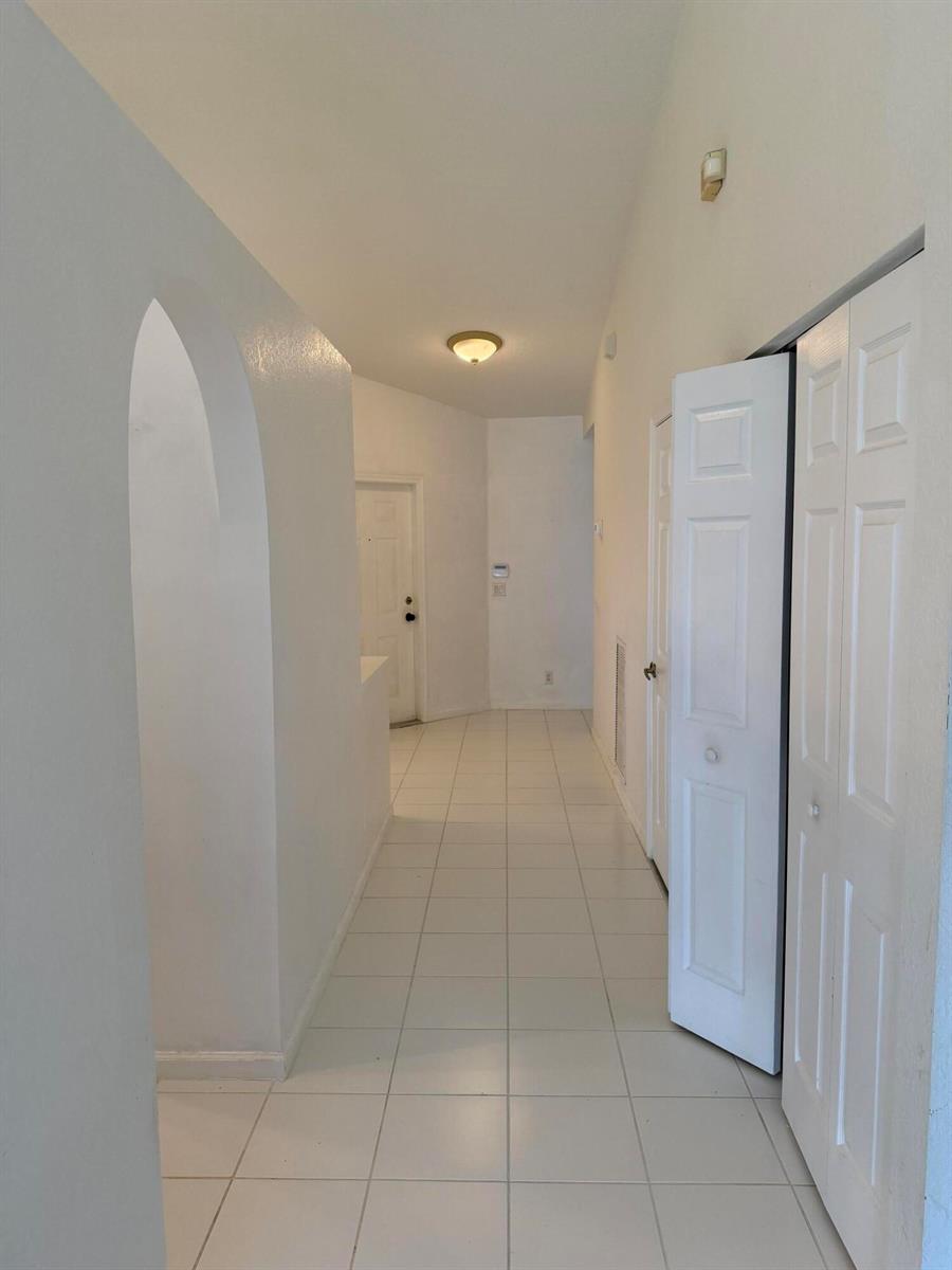 A white-tiled hallway features an arched entryway, white walls, and several closed closet doors — 8432 Cargill Point, West Palm Beach FL 33411, WEST PALM BEACH, FL