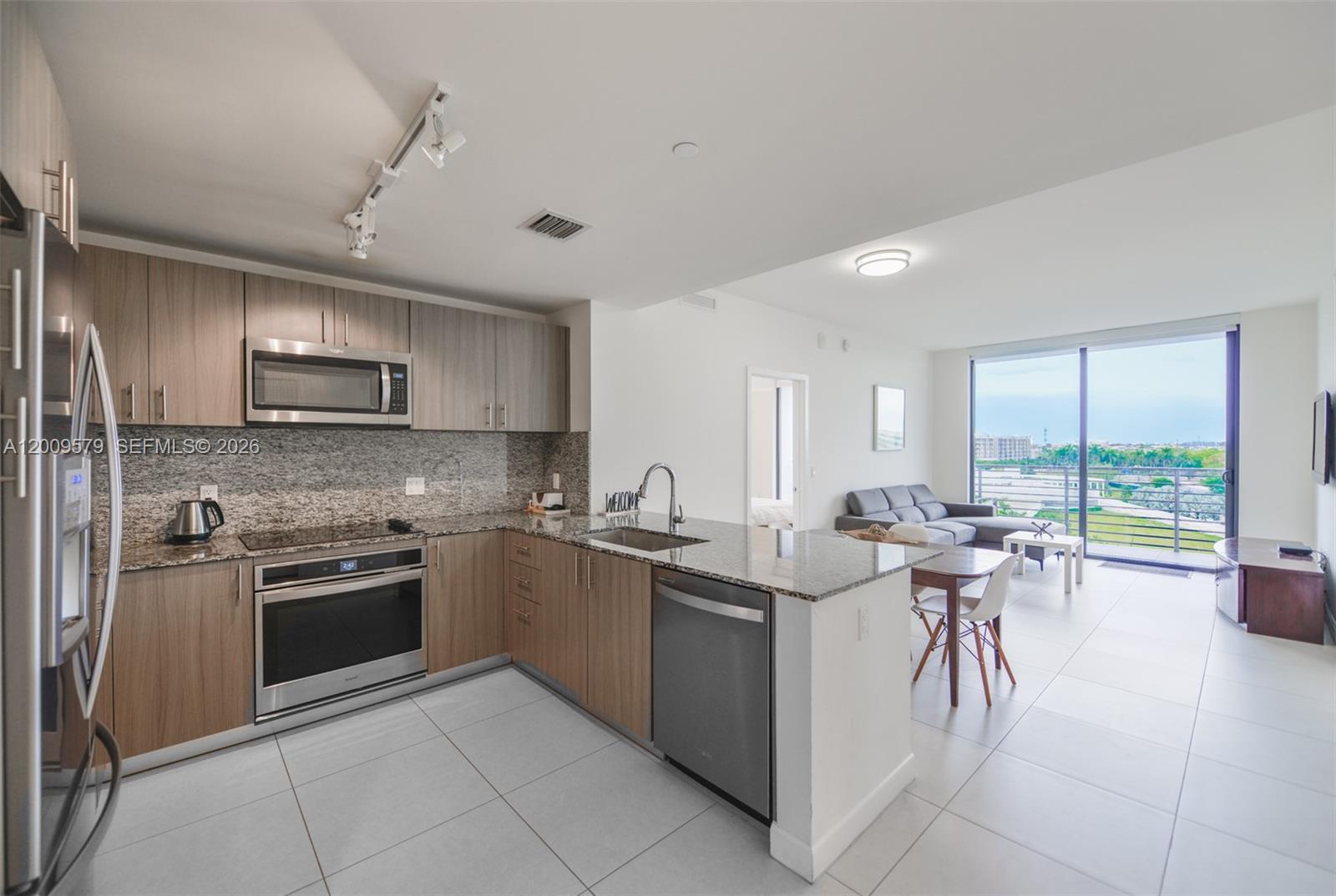 A modern kitchen with wood cabinets and granite countertops opens to a living area — 5350 NW 84th Ave # 509, Doral FL 33166, DORAL, FL