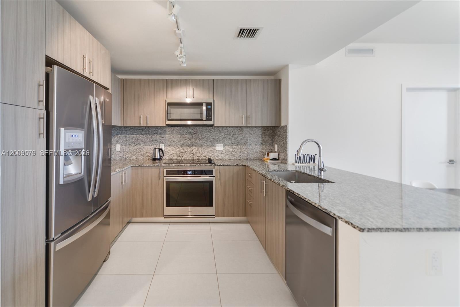 A modern kitchen features light wood cabinets, stainless steel appliances, and granite countertops — 5350 NW 84th Ave # 509, Doral FL 33166, DORAL, FL
