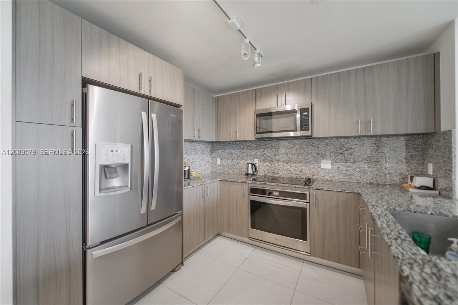A modern kitchen features light wood cabinets, stainless steel appliances, and speckled granite countertops — 5350 NW 84th Ave # 509, Doral FL 33166, DORAL, FL
