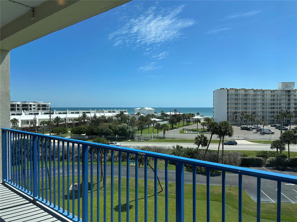 A balcony with a blue metal railing overlooks a parking lot, palm trees, and the ocean — 5300 S ATLANTIC AVENUE UNIT 3-504, NEW SMYRNA BEACH, FL