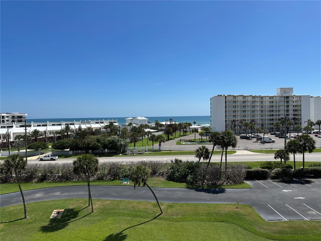 An elevated view of a coastal parking lot, palm trees, and a multi-story apartment building — 5300 S ATLANTIC AVENUE UNIT 3-504, NEW SMYRNA BEACH, FL