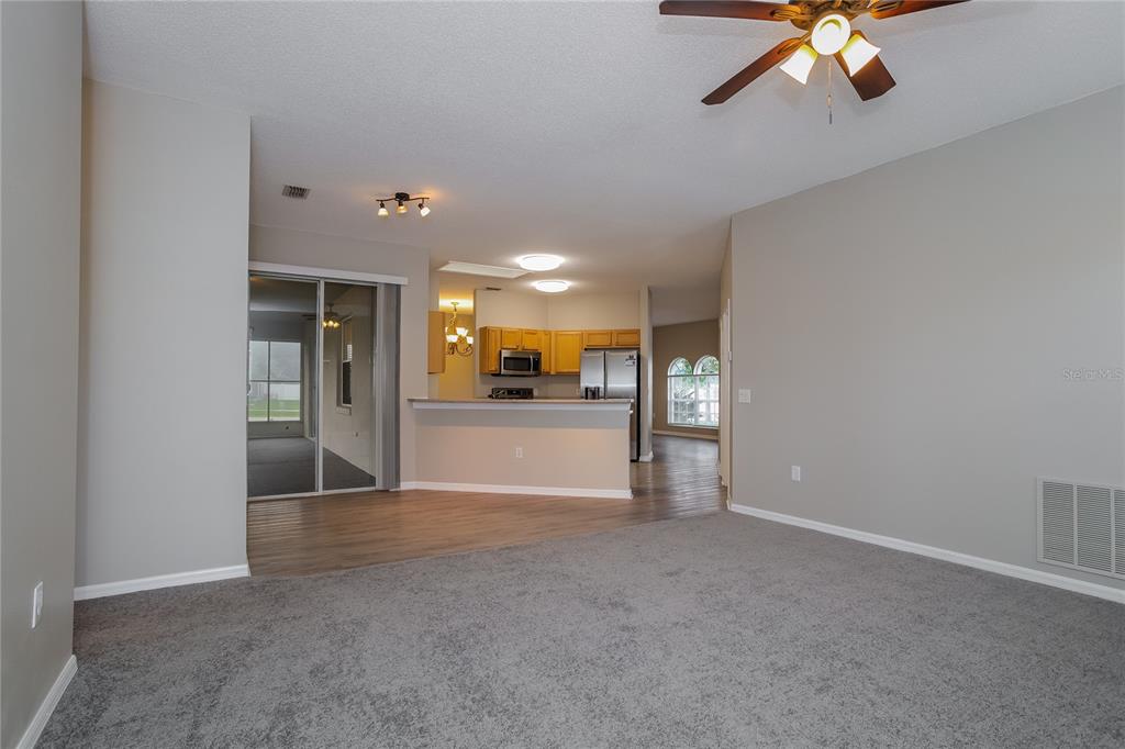 A living room with gray carpet transitions to wood-look flooring in an open-concept kitchen area — 421 PEPPERMILL CIRCLE, KISSIMMEE, FL