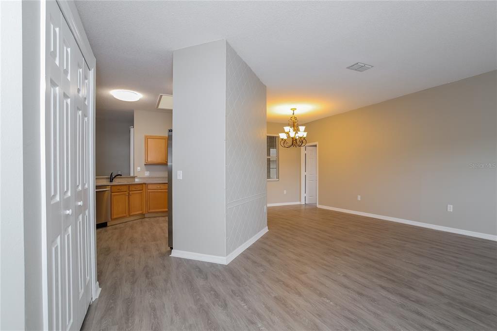 An open-concept living area features light wood-look flooring, a central accent wall, and a kitchen — 421 PEPPERMILL CIRCLE, KISSIMMEE, FL