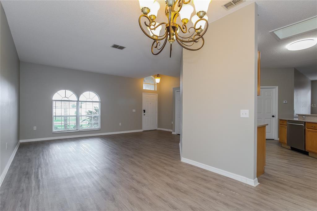 An open-concept living area features light gray walls, wood-look flooring, and a decorative chandelier — 421 PEPPERMILL CIRCLE, KISSIMMEE, FL