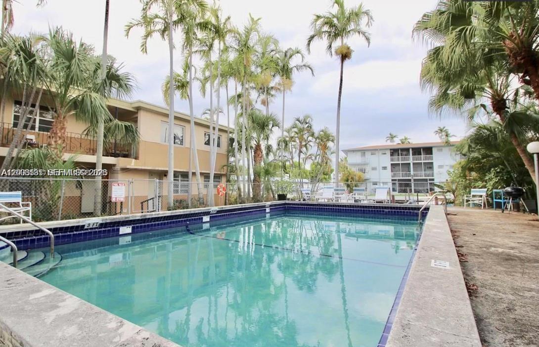 A rectangular swimming pool is surrounded by palm trees and multi-story apartment buildings — 645 NE 77th St # 16, Miami FL 33138, MIAMI, FL