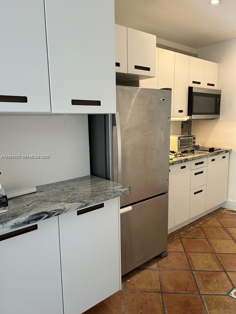 A kitchen features white cabinets, stainless steel appliances, granite countertops, and terracotta tile flooring — 645 NE 77th St # 16, Miami FL 33138, MIAMI, FL