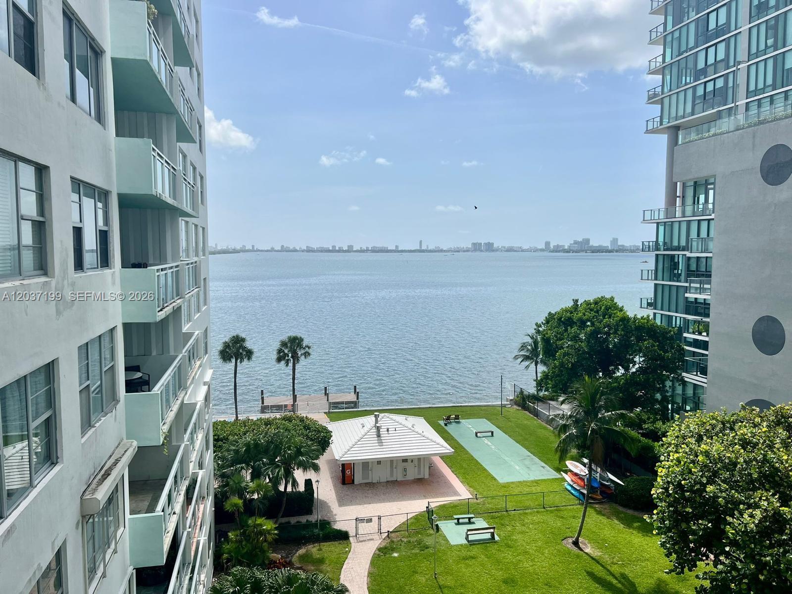 An elevated view of a waterfront courtyard with a small building, lawn, and boat dock — 3301 NE 5th Ave # 706, Miami FL 33137, MIAMI, FL