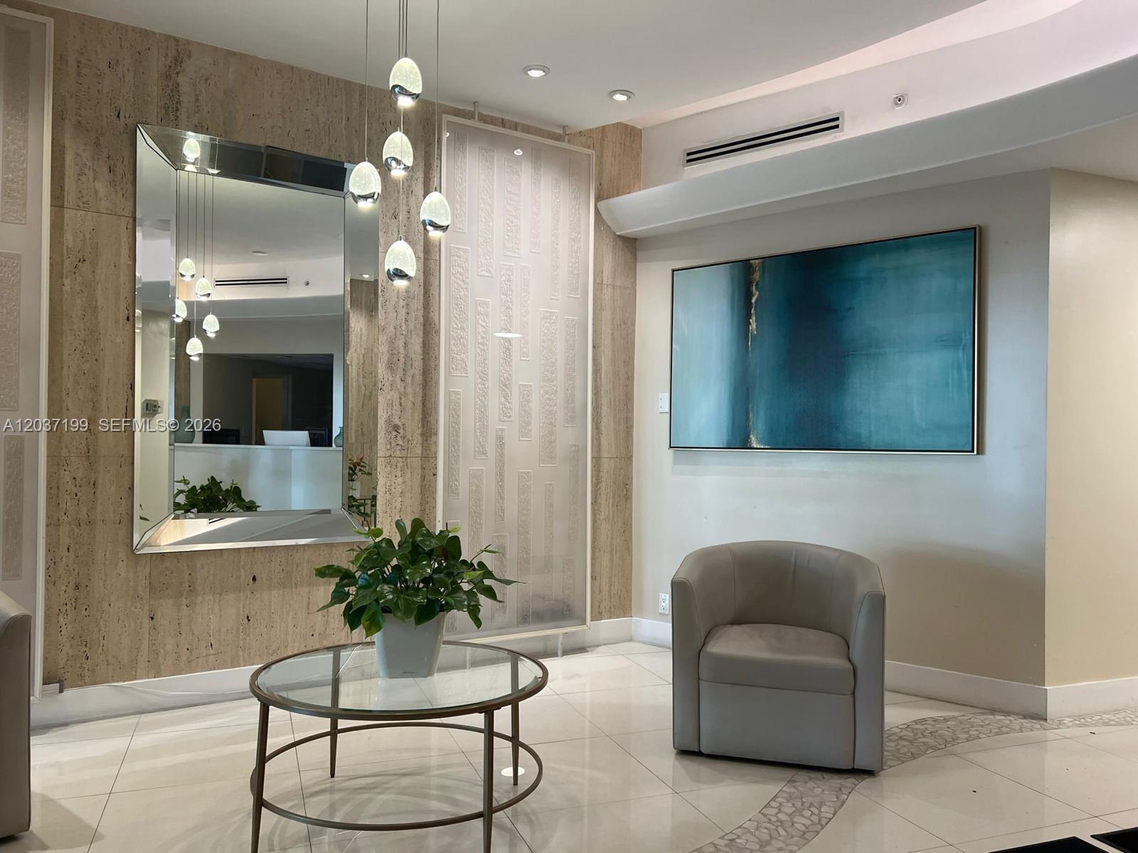 A modern lobby features a glass table, a gray armchair, a large mirror, and artwork — 3301 NE 5th Ave # 706, Miami FL 33137, MIAMI, FL