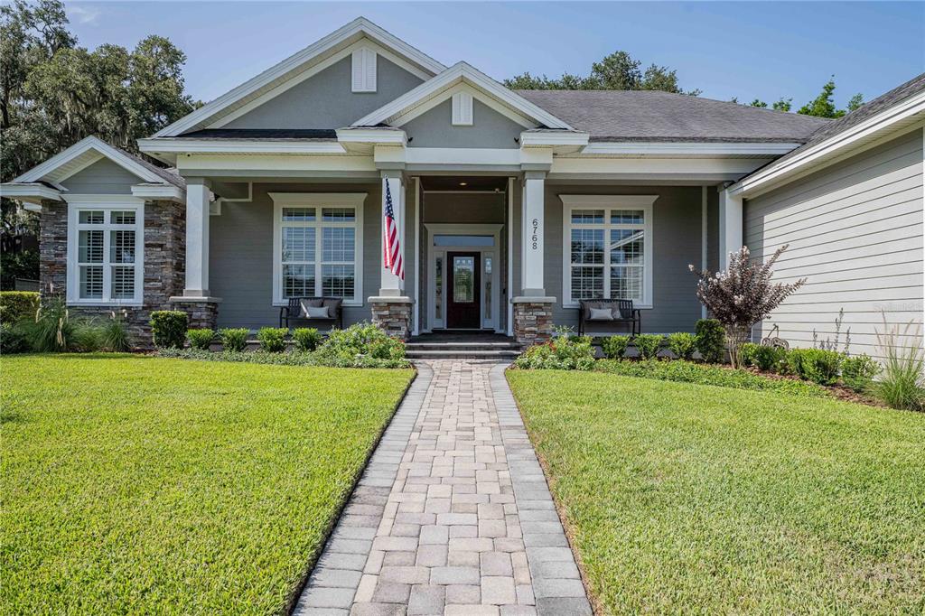 A gray house with a stone-accented facade and a paved walkway leading to the entrance — 6768 CRESCENT WOODS CIRCLE, LAKELAND, FL