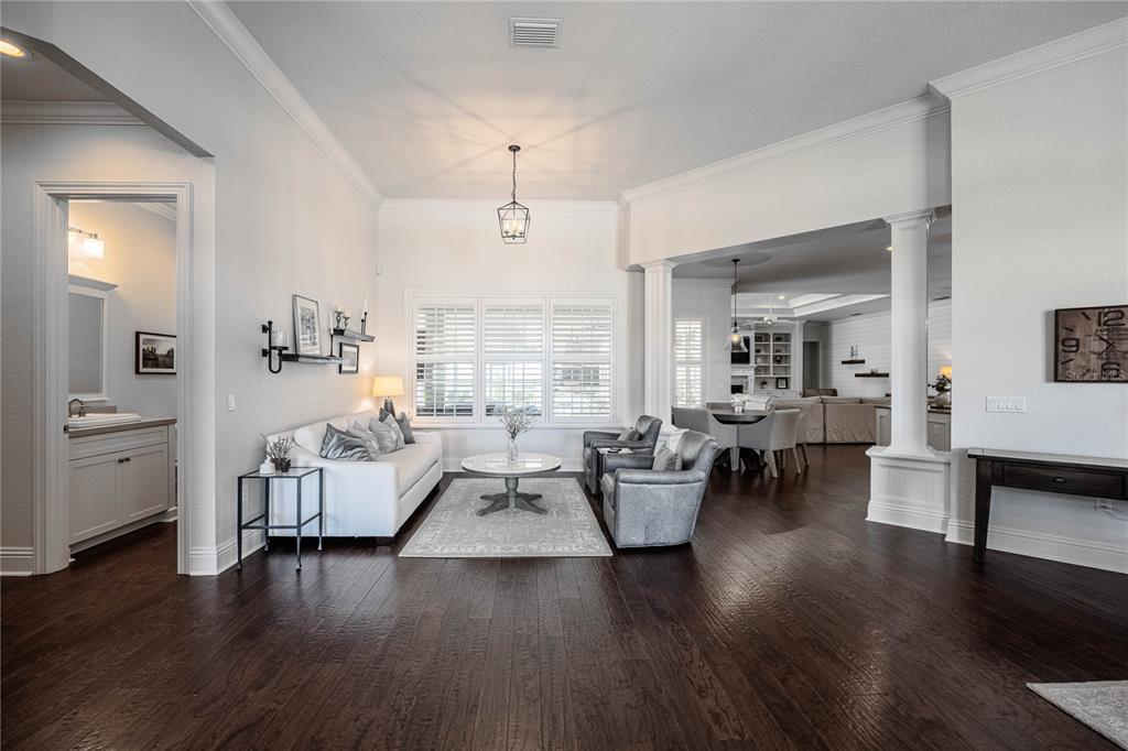 A living room with dark hardwood floors, white walls, a white sofa, and two armchairs — 6768 CRESCENT WOODS CIRCLE, LAKELAND, FL