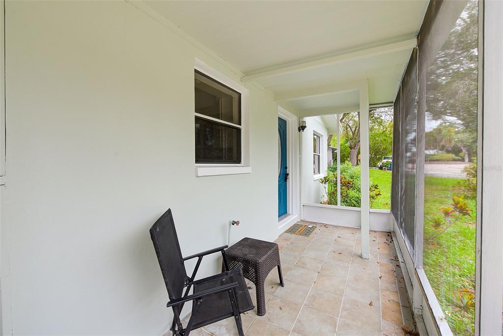 A screened-in porch with tiled flooring, a black chair, a small table, and a blue door — 1011 FAIRMONT STREET, CLEARWATER, FL