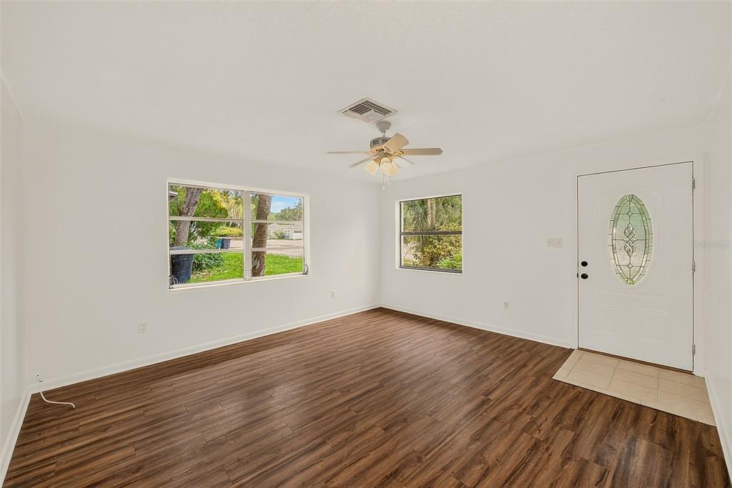 An empty living room features white walls, wood-look flooring, a ceiling fan, and a front door — 1011 FAIRMONT STREET, CLEARWATER, FL