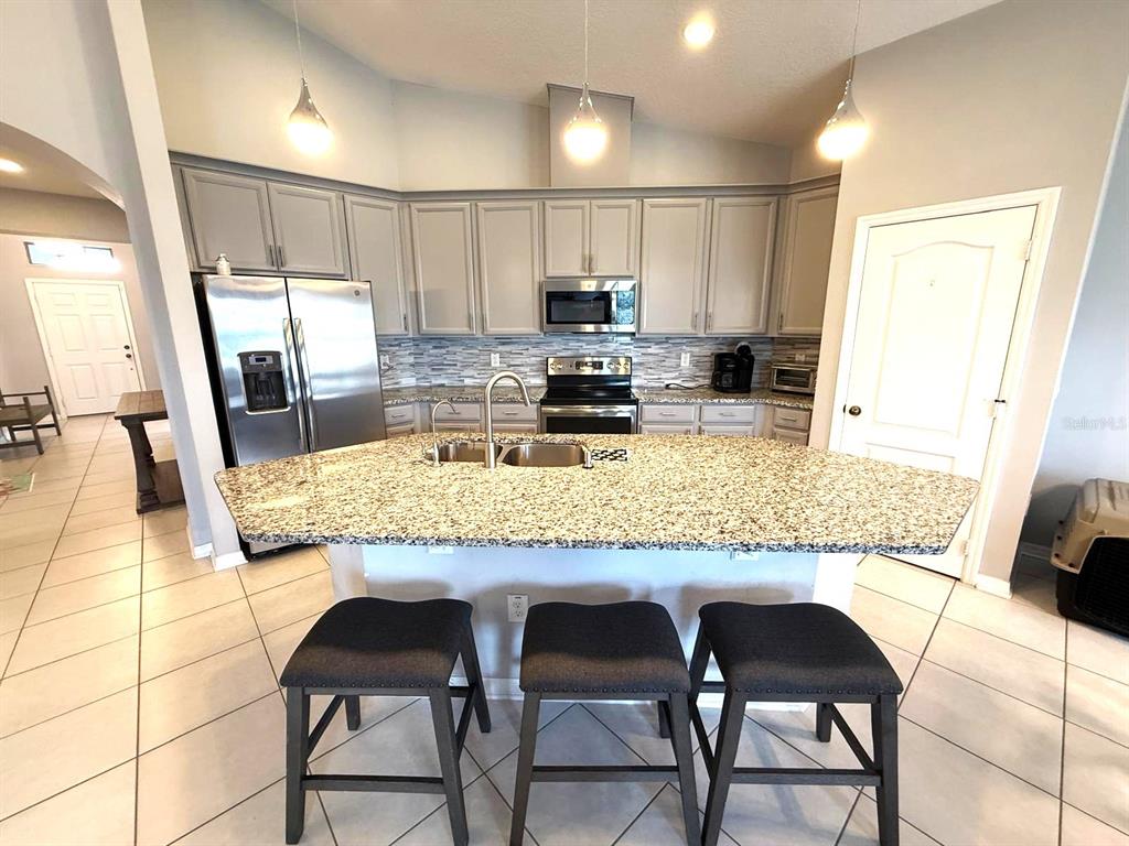 A kitchen features gray cabinets, granite countertops, a central island with seating, and tile flooring — 1165 HILLTOP PLACE, ST CLOUD, FL