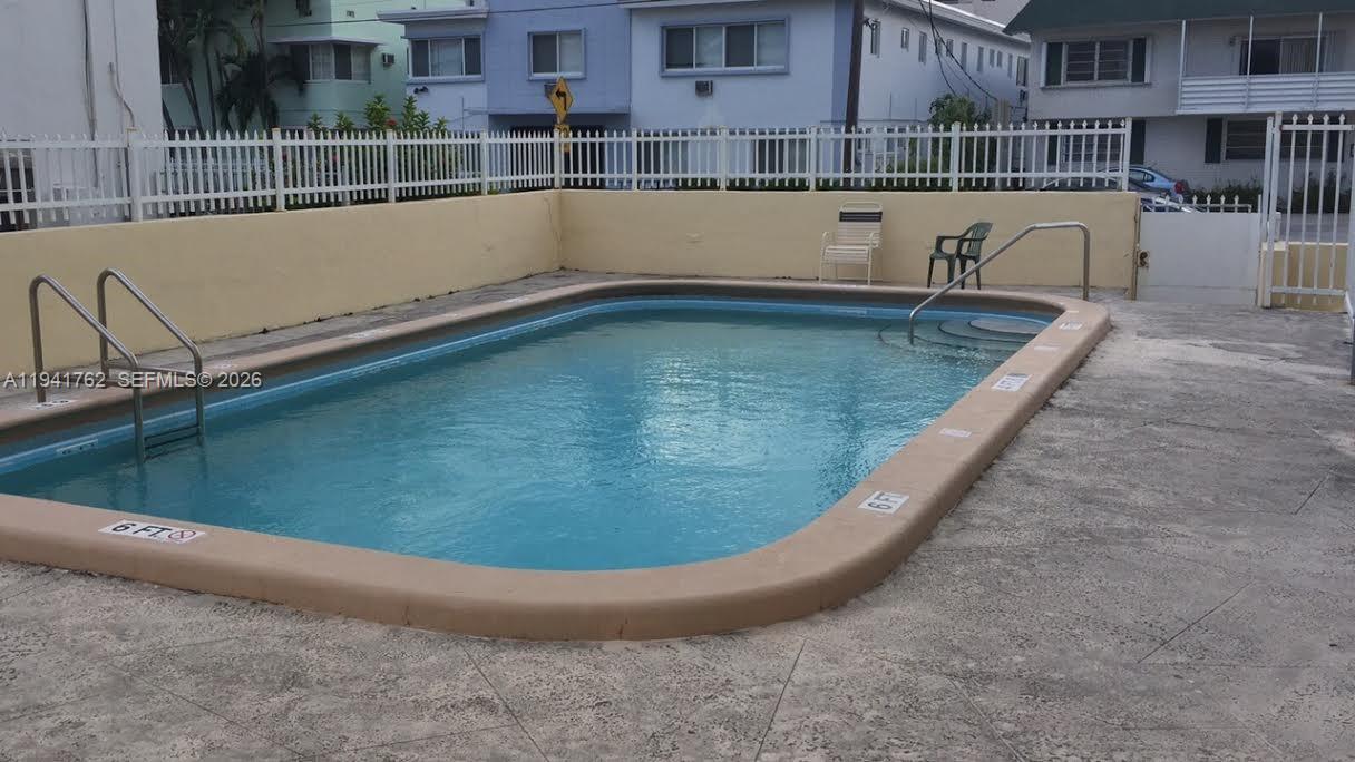 An outdoor swimming pool with a tan coping and metal ladders sits in a courtyard — 6855 Abbott Ave # 601, Miami Beach FL 33141, MIAMI BEACH, FL