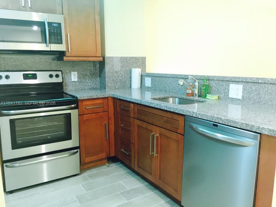 A kitchen features wood cabinets, granite countertops, stainless steel appliances, and light tile flooring — 6855 Abbott Ave # 601, Miami Beach FL 33141, MIAMI BEACH, FL