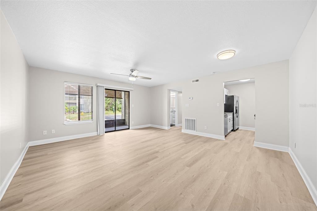 An empty living room features light wood-look flooring, a ceiling fan, and a sliding glass door — 3545 SABLE PALM LANE UNIT B, TITUSVILLE, FL