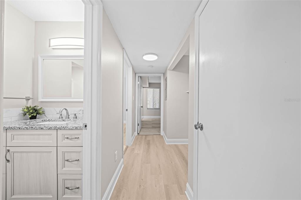 A hallway with light wood flooring leads to a bedroom, with a bathroom vanity on the left — 3545 SABLE PALM LANE UNIT B, TITUSVILLE, FL
