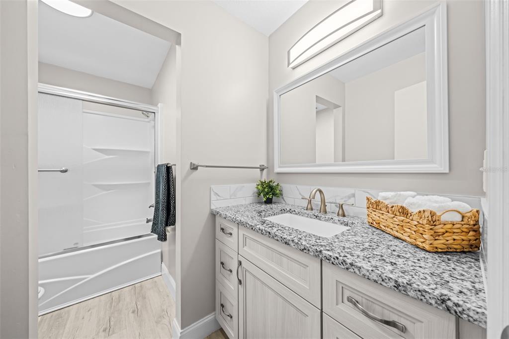 A bathroom features a granite vanity, a white cabinet, a mirror, and a shower-tub combo — 3545 SABLE PALM LANE UNIT B, TITUSVILLE, FL