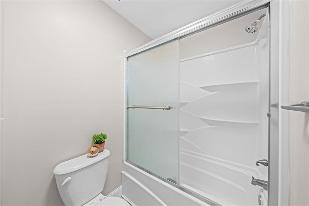 A bathroom features a white toilet next to a shower with a frosted glass sliding door — 3545 SABLE PALM LANE UNIT B, TITUSVILLE, FL