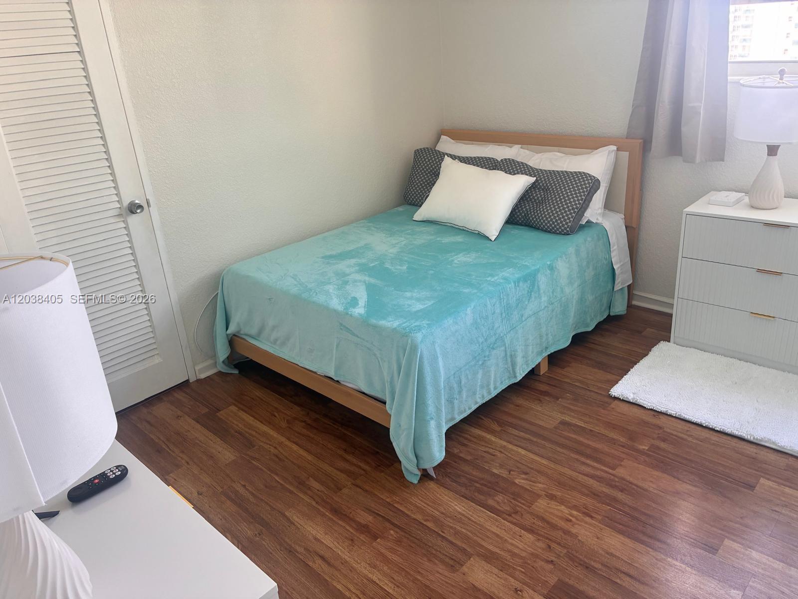 A bedroom features a bed with a teal blanket, wood flooring, and a white dresser — 3901 S Ocean Dr # 14Q, Hollywood FL 33019, HOLLYWOOD, FL