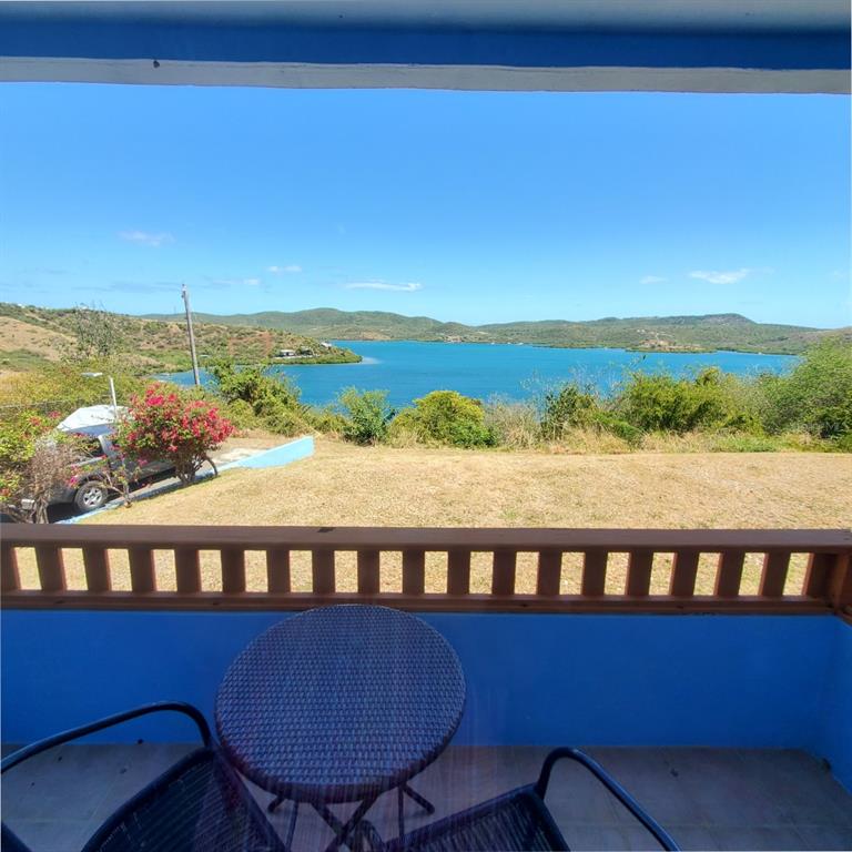 A view from a blue balcony overlooking a grassy yard, a parked car, and the ocean — D101 BAHIA MARINA CONDOMINIUM RESORT UNIT D101, CULEBRA, PR