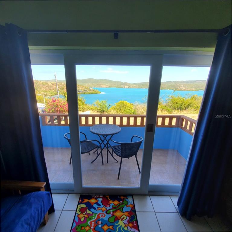 A view of a balcony with a table and chairs overlooking a bay through sliding doors — D101 BAHIA MARINA CONDOMINIUM RESORT UNIT D101, CULEBRA, PR