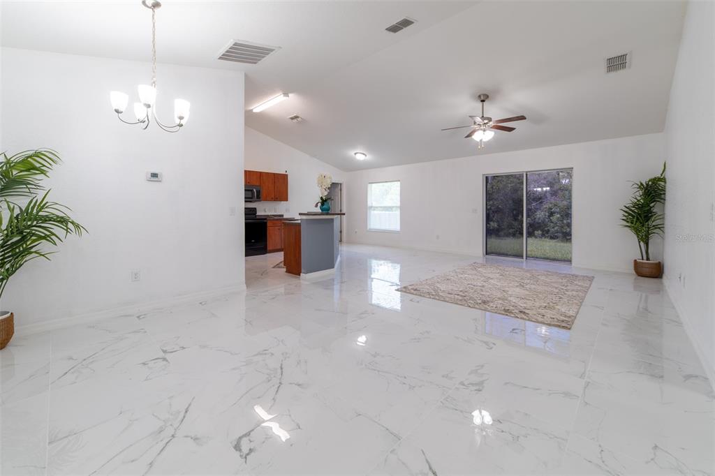 An open-concept living and dining area features white marble-look tile flooring and a kitchen island — 5107 SW 165TH STREET ROAD, OCALA, FL