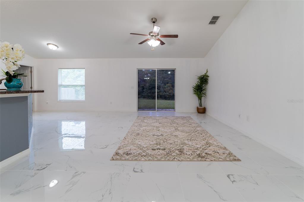 A bright living room features white marble-look tile flooring, a ceiling fan, and sliding glass doors — 5107 SW 165TH STREET ROAD, OCALA, FL