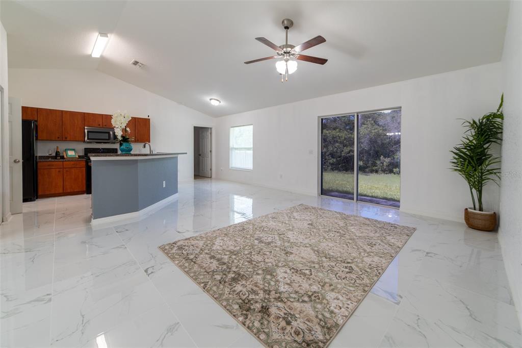 An open-concept living area features white marble-look tile floors, a kitchen island, and sliding doors — 5107 SW 165TH STREET ROAD, OCALA, FL