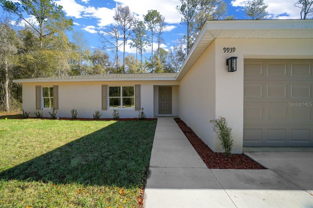 A single-story house with a beige exterior, a gray garage door, and a concrete walkway — 9939 N ATHENIA DRIVE, CITRUS SPRINGS, FL