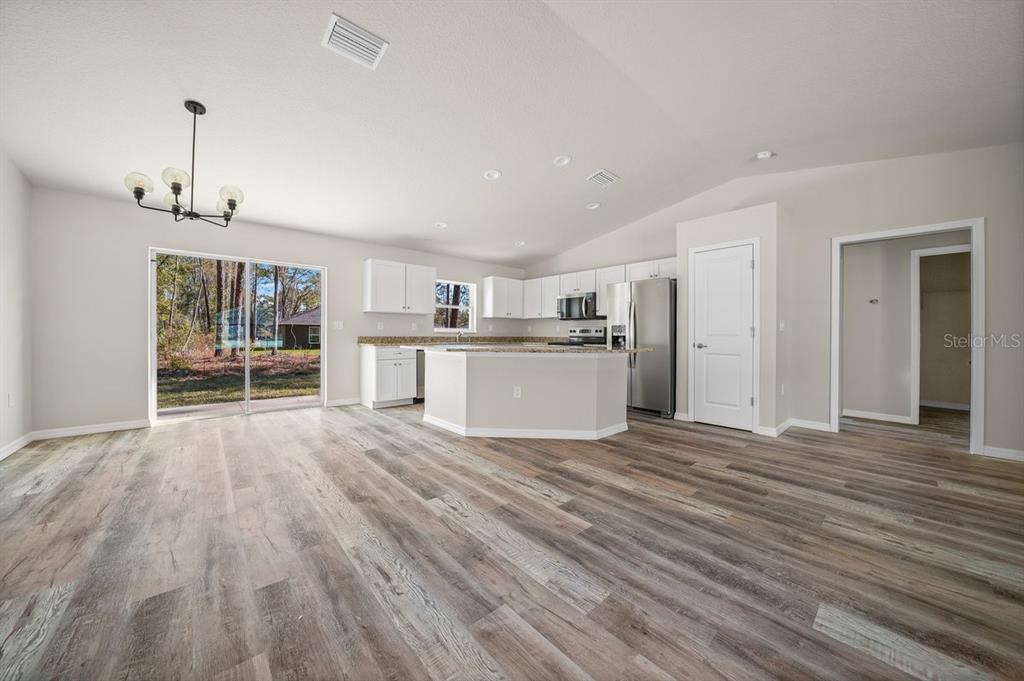 An open-concept kitchen and living area features light wood-look flooring, white cabinets, and sliding doors — 9939 N ATHENIA DRIVE, CITRUS SPRINGS, FL