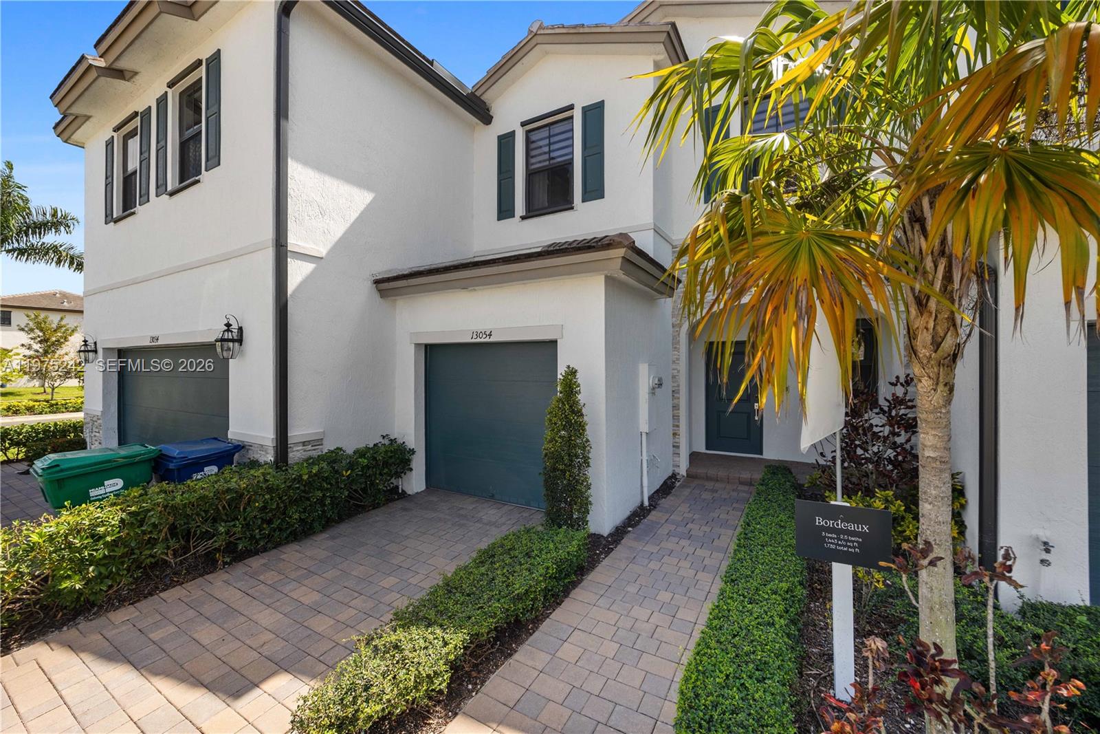 A two-story townhouse exterior features a single-car garage, a paved walkway, and a small palm tree — 13054 SW 233rd Ter, Homestead FL 33032, HOMESTEAD, FL