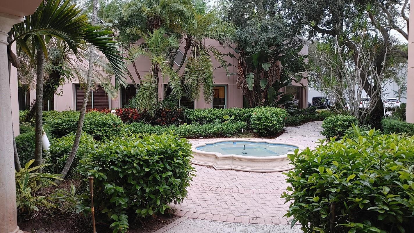 A stone fountain sits in a landscaped courtyard in front of a pink building — 1565 N Park Drive # 104, Weston FL 33326, WESTON, FL