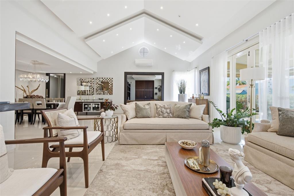 A bright living room features a vaulted ceiling, neutral furniture, and large glass sliding doors — 147 CAMINO DE LOS JUNCOS, DORADO, PR