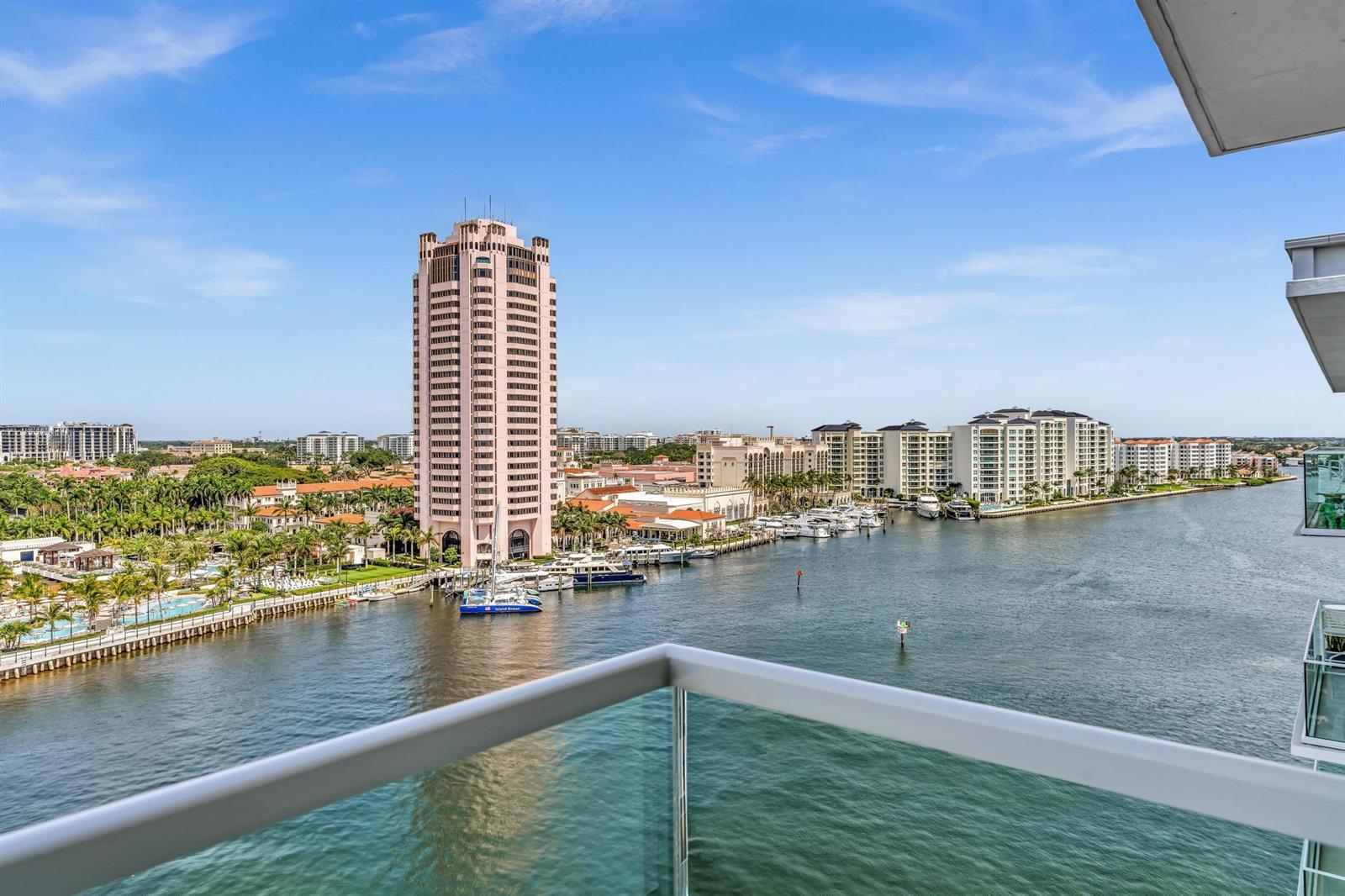 A high-angle view from a balcony overlooking a waterway, a tall pink tower, and buildings — 701 E Camino Real # 12g, Boca Raton FL 33432, BOCA RATON, FL