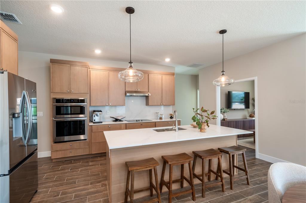 A modern kitchen features light wood cabinets, a white island with bar stools, and stainless appliances — 3563 NW 45TH AVENUE, OCALA, FL